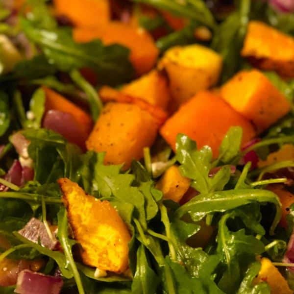 a closeup of roasted butternut squash salad over arugula