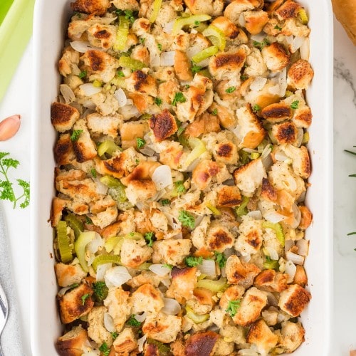 Homemade Stuffing in a white baking dish made with toasted bread cubes, celery, onions, and fresh herbs.