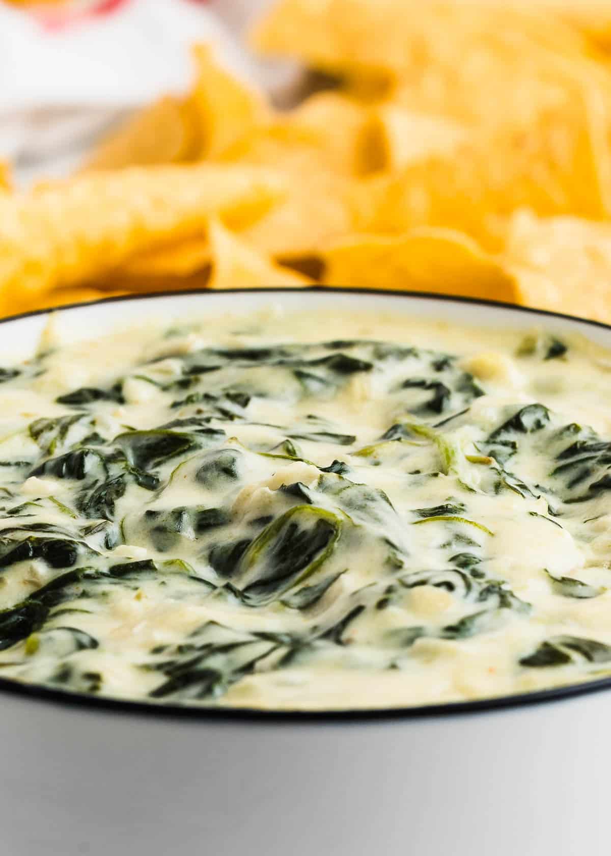 Creamy Spinach Dip in a white bowl served with tortilla chips.