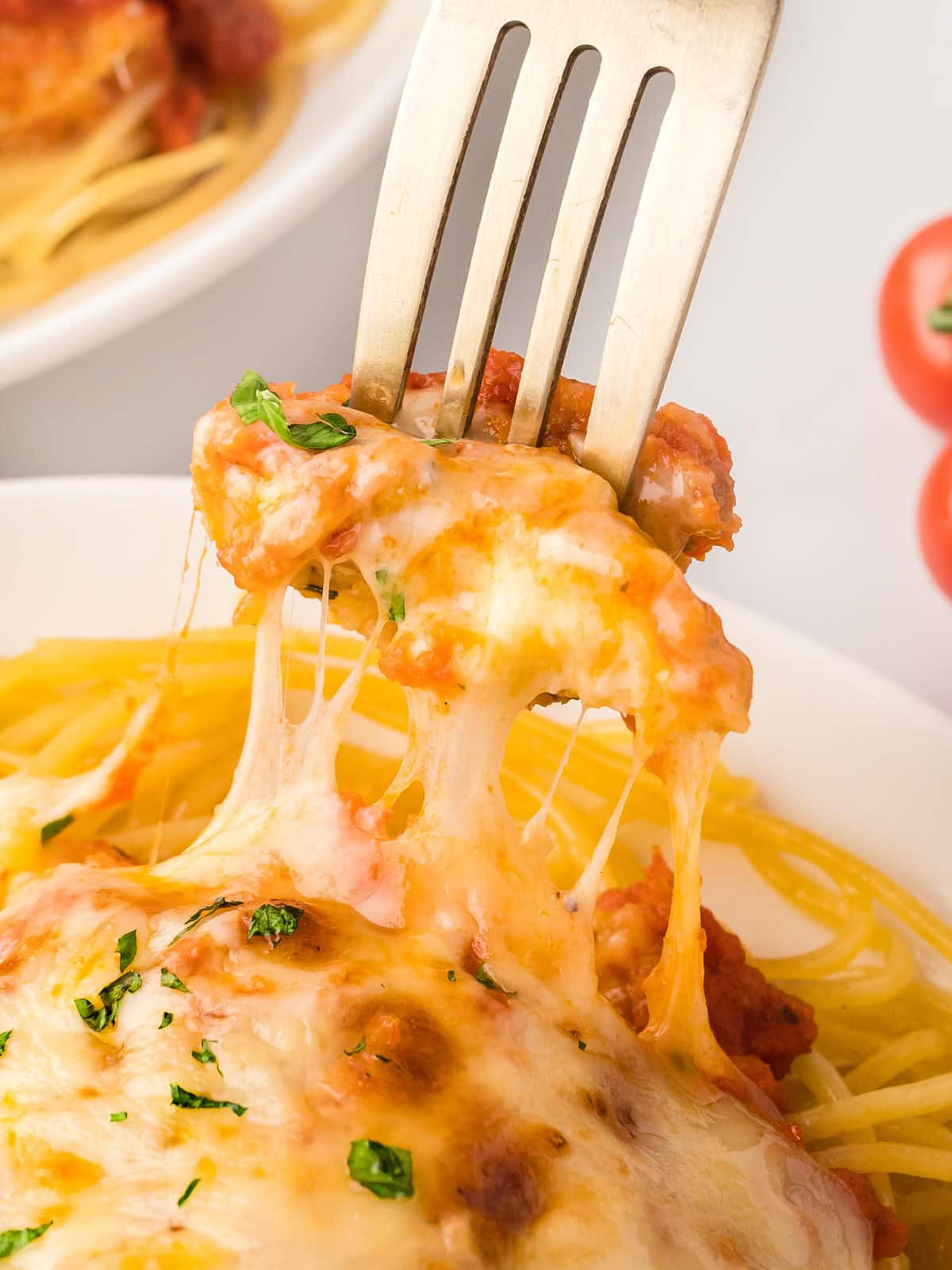 A fork is being used to eat a plate of spaghetti topped with Chicken Parmesan.