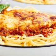 Chicken Parmesan served over spaghetti in a white bowl.