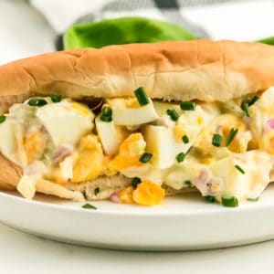 a closeup of classic egg salad in a bread bun on a white plate