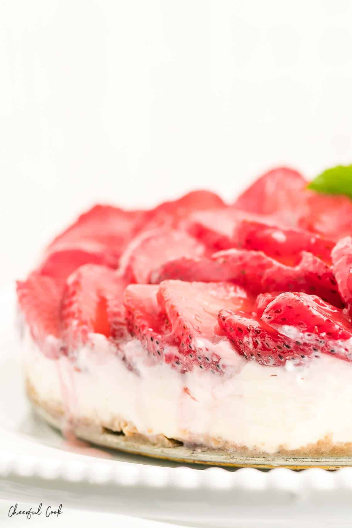 A closeup image of the no bake strawberry cheesecake placed on a white cake stand. 