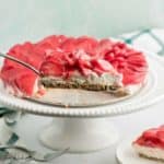 A slice of no bake strawberry cheesecake taken off a white cake stand