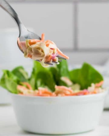 a forkful of creamy cole slaw out of a white bowl