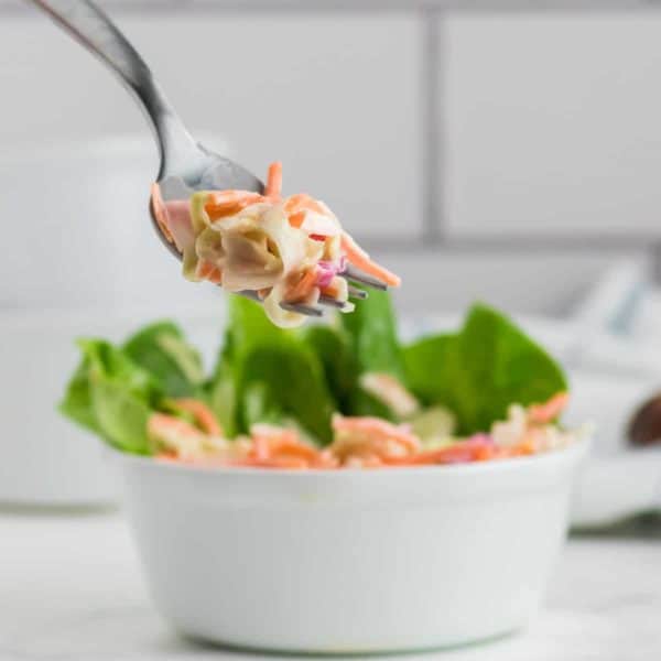 A forkful of Creamy Coleslaw out of a white bowl.