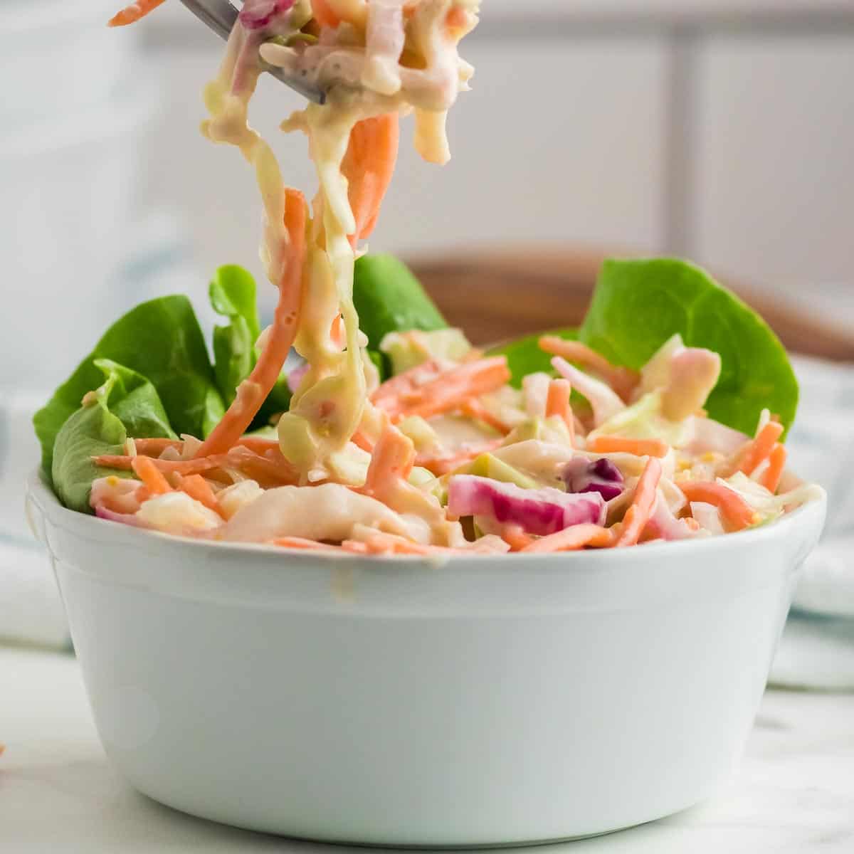 a forkful of freshly made creamy coleslaw in a white bowl