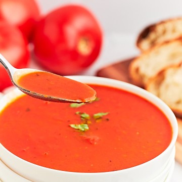 A spoonful of freshly cooked rustic Tomato Soup served in a white bowl.