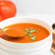 A spoonful of freshly cooked tomato soup served in a white bowl.