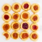 16 freshly baked Thumbprint Cookies (German Engelsaugen) with one cheeky bite taken out of one cookie
