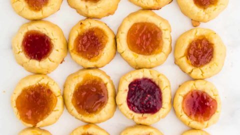 16 freshly baked Thumbprint Cookies (German Engelsaugen) with one cheeky bite taken out of one cookie