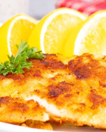 closeup image of freshly fried chicken schnitzel served with sliced lemons