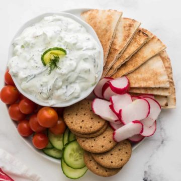 Cucumber Dip in a bowl served on a platter of fresh veggies, crackers, and pita bread.