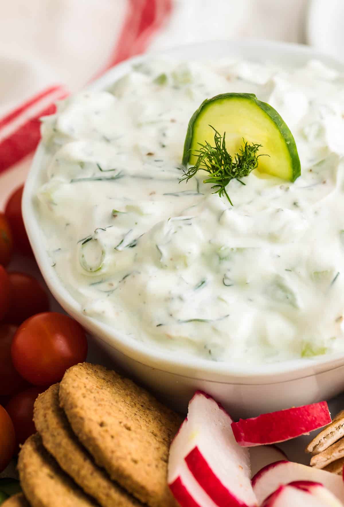 closeup of.image of freshly made Cucumber Dip in a white bowl sitting on a veggie and cracker platter