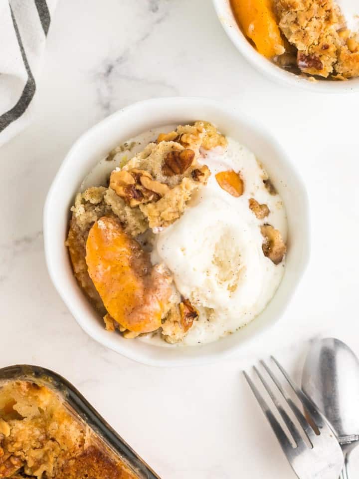 peach dump cake in a white bowl topped with vanilla ice cream