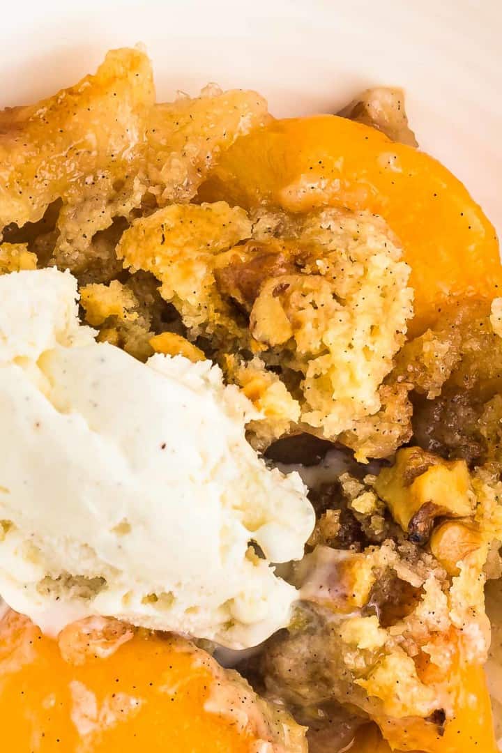 closeup image of a freshly baked peach dump cake topped with a scoop of vanilla ice cream