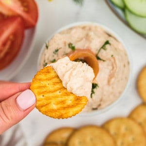 Closeup of a wheat cracker dipping in smoked salmon dip.