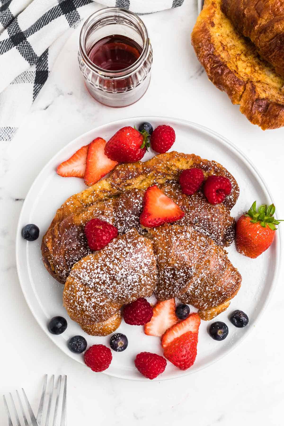 a plate of croissant french toast dusted with confectioner's sugar and served with berries