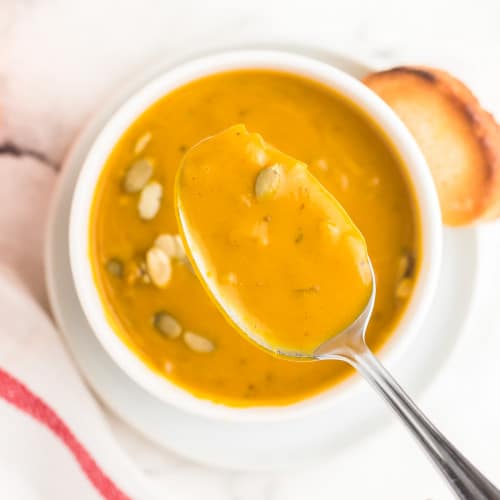 A spoonful of last minute pumpkin soup taken from a white bowl.