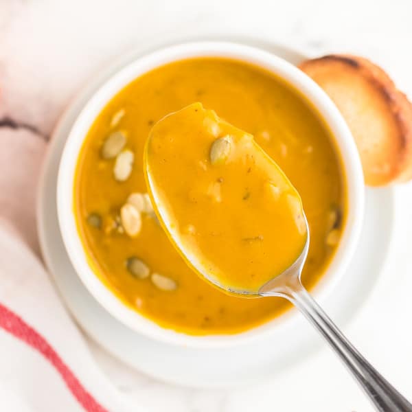 A spoonful of last minute pumpkin soup taken from a white bowl.