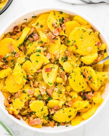 Warm German Potato Salad with bacon in a white bowl.