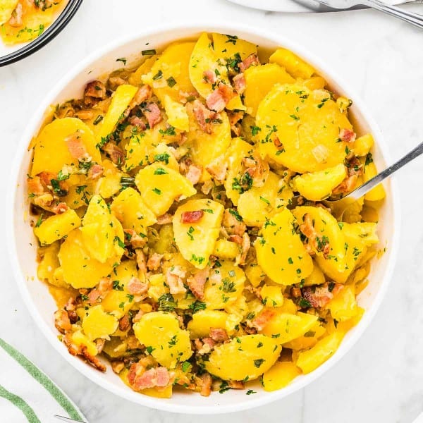 Warm German Potato Salad with bacon in a white bowl.