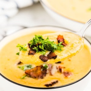 A spoonful of Butternut Squash Soup topped with bacon and parsley.