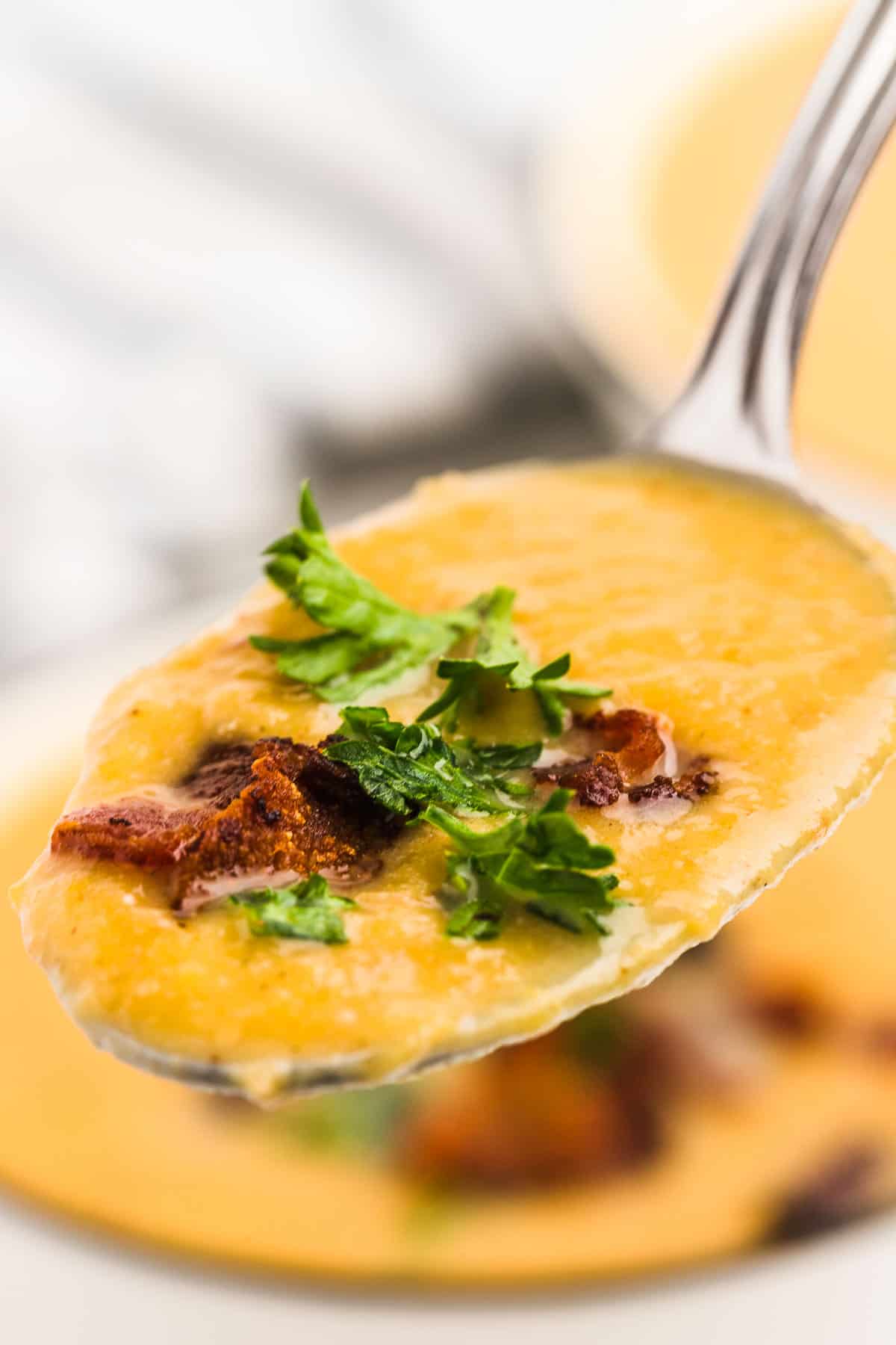 A spoonful of Butternut Squash Soup garnished with bacon and fresh parsley.