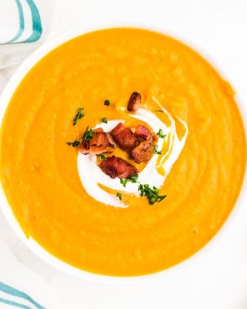 Sweet Potato Soup topped with bacon, parsley, and sour cream in a white bowl.