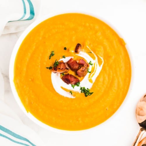 Sweet Potato Soup topped with bacon, parsley, and sour cream in a white bowl.
