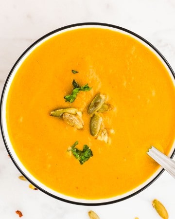 A bowl of Pumpkin Curry Soup garnished with fresh parsley and roasted pumpkin seeds.