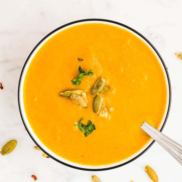 A bowl of Pumpkin Curry Soup garnished with fresh parsley and roasted pumpkin seeds.