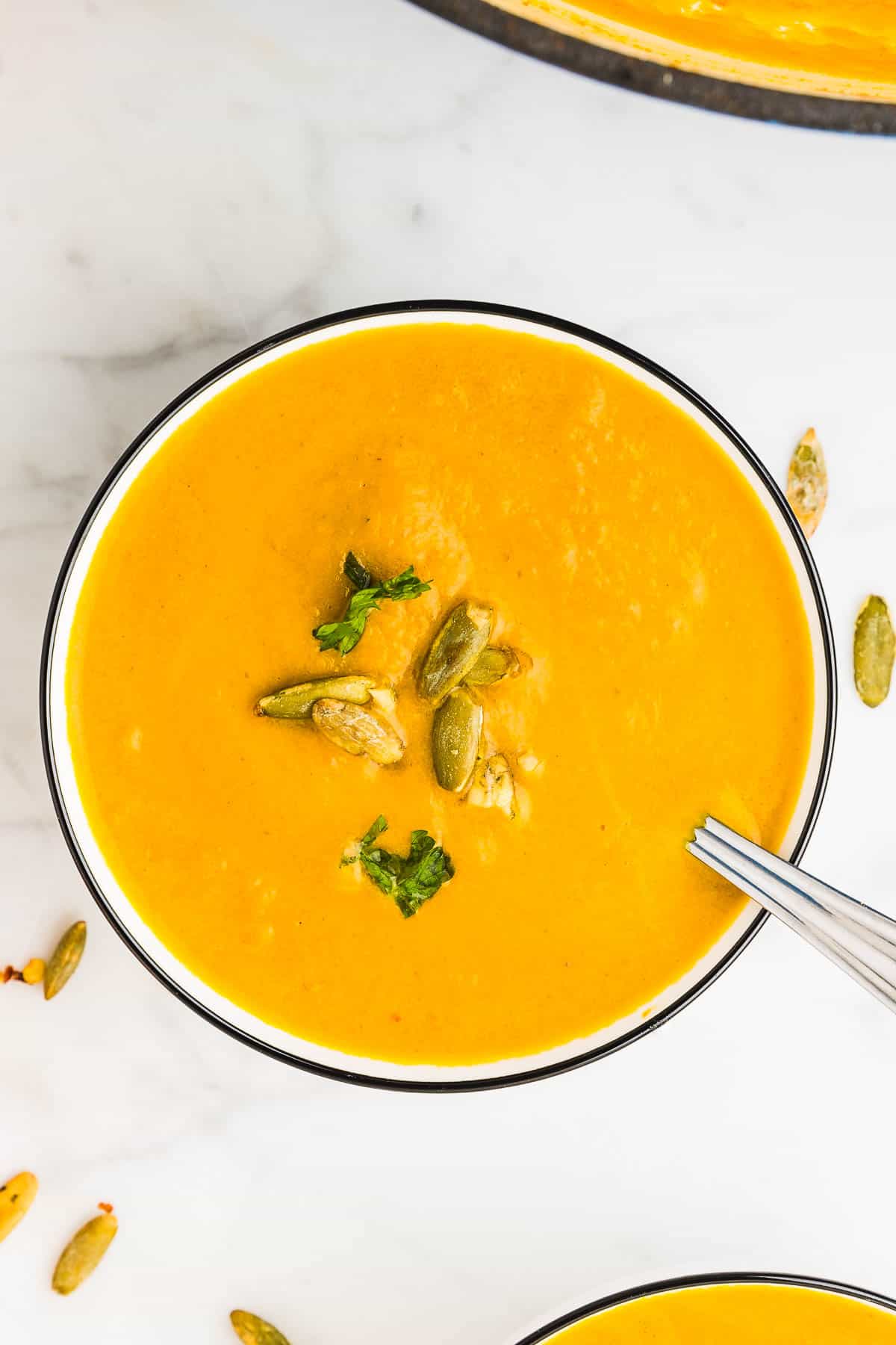 A bowl of Pumpkin Curry Soup garnished with fresh parsley and roasted pumpkin seeds.