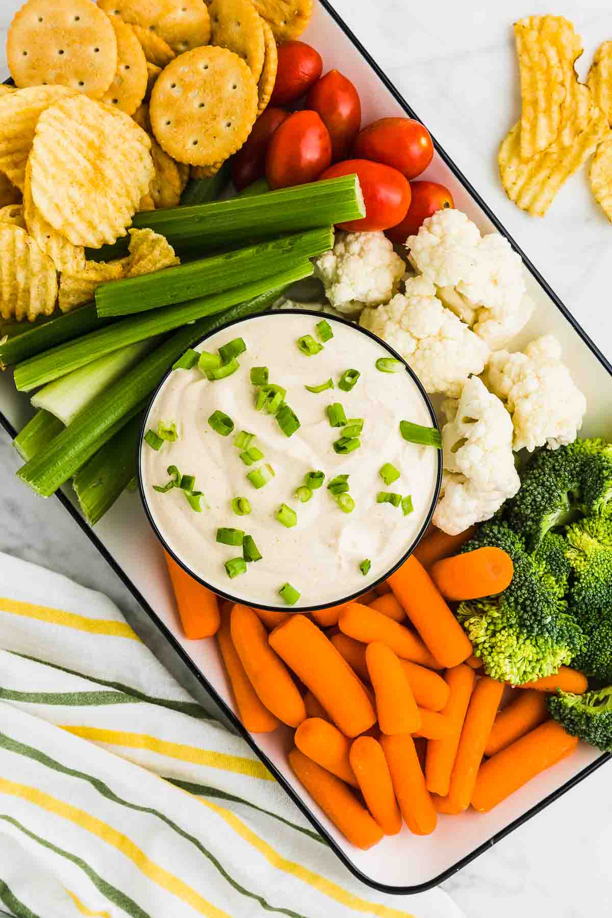 A bowl of Curry Dip on a plate of veggies, crackers, and chips.
