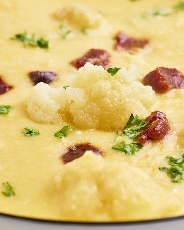 Closeup of a cheesy Cauliflower Soup in a white bowl.