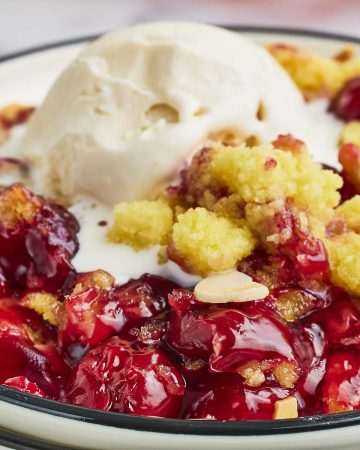 Closeup of a slice of Cherry Dump Cake with a scoop of vanilla ice cream on a white plate.
