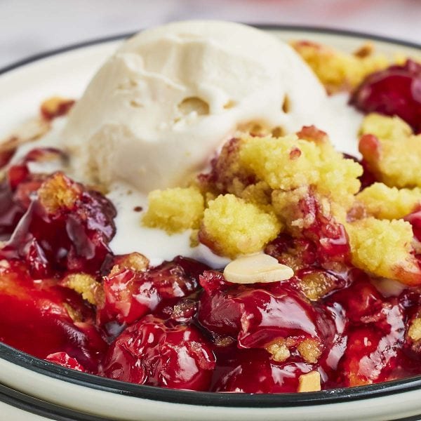 Closeup of a slice of Cherry Dump Cake with a scoop of vanilla ice cream on a white plate.