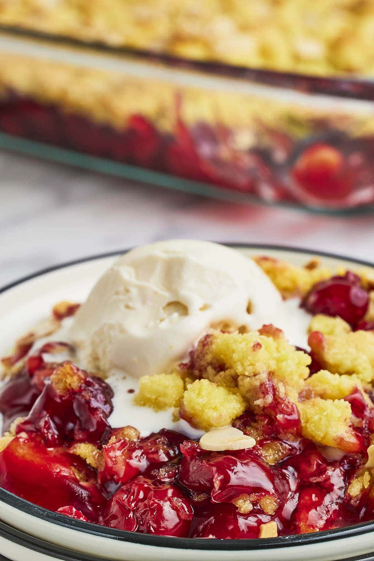 Closeup of a Cherry Dump Cake served on a white plate with vanilla ice cream.