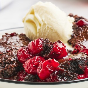 Closeup of a Black Forest Dump Cake with a scoop of vanilla ice cream on a white plate.
