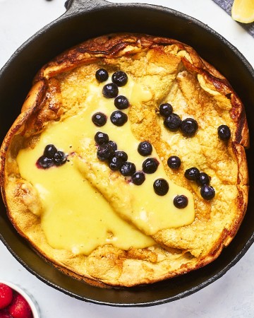 Topdown view of a Dutch baby in a cast iron skillet topped with lemon curd and fresh blueberries.