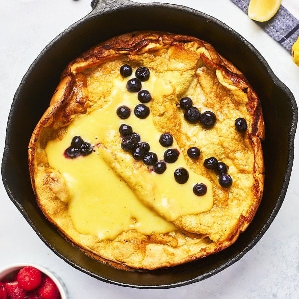 Topdown view of a Dutch baby in a cast iron skillet topped with lemon curd and fresh blueberries.