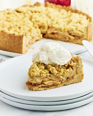 A slice of German Apple Cake topped with whipped cream on a white plate.