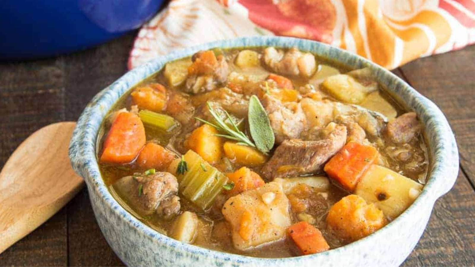 A bowl of pork stew with potatoes and squash cubes.