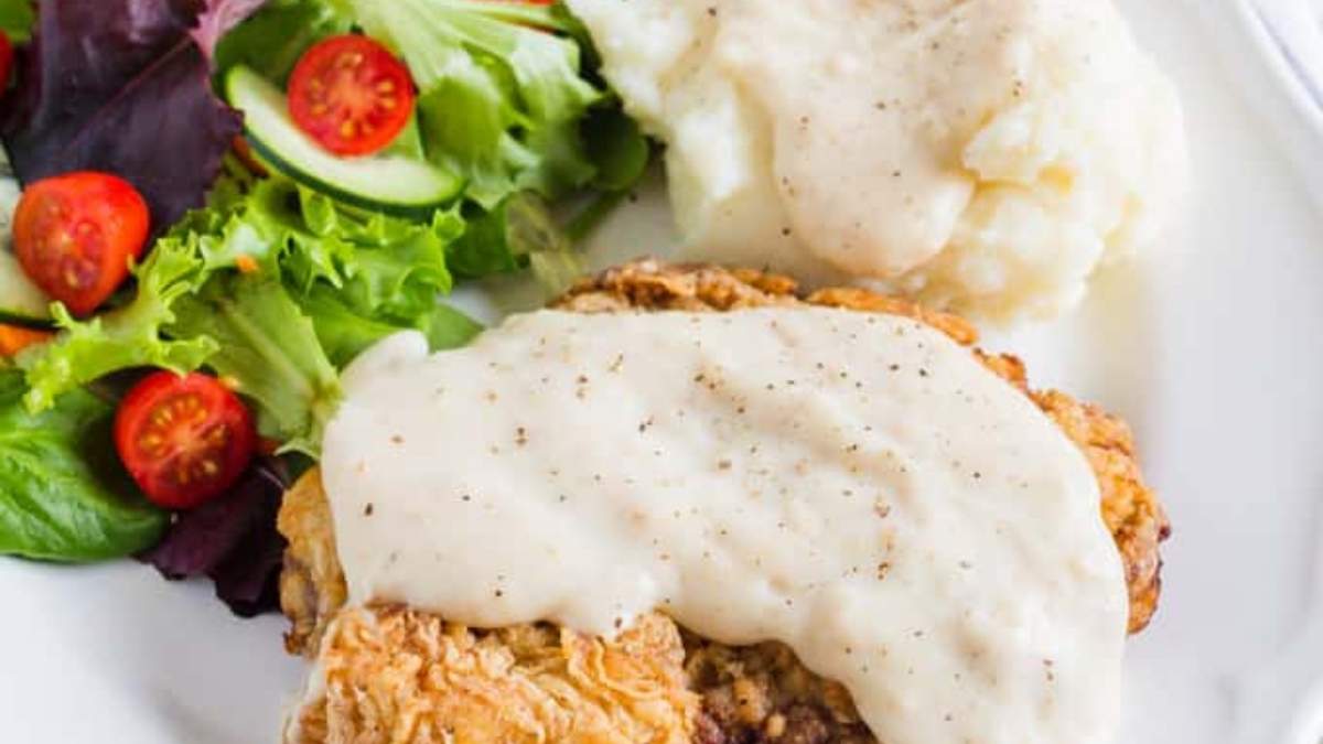 Chicken fried steak with gravy and mashed potatoes on a white plate.