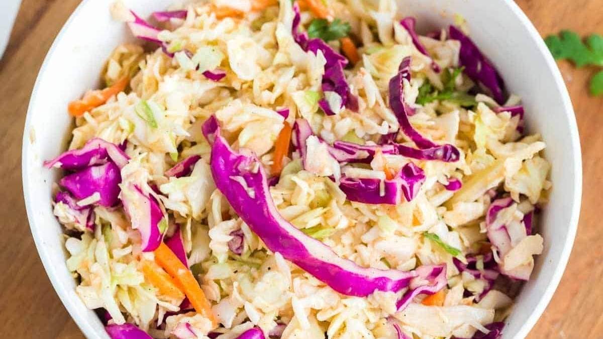Coleslaw in a white bowl on a wooden table.