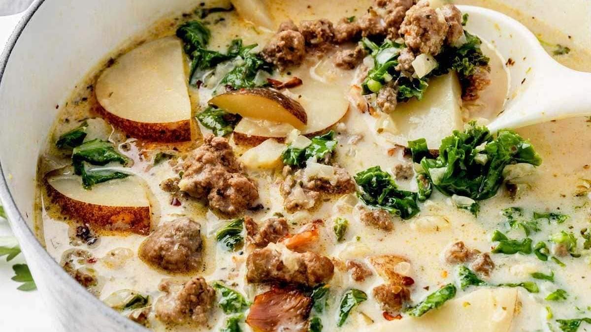 A pot of soup with meat, potatoes and kale.