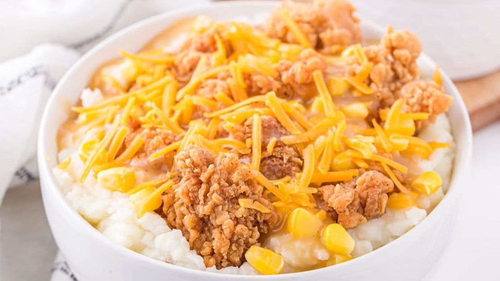 A bowl of mashed potatoes, chicken, corn, and cheese.