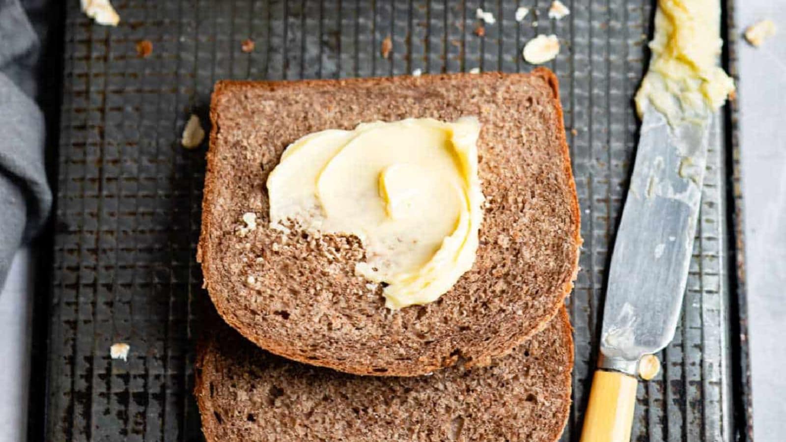A loaf of brown bread, sliced and spread with butter.