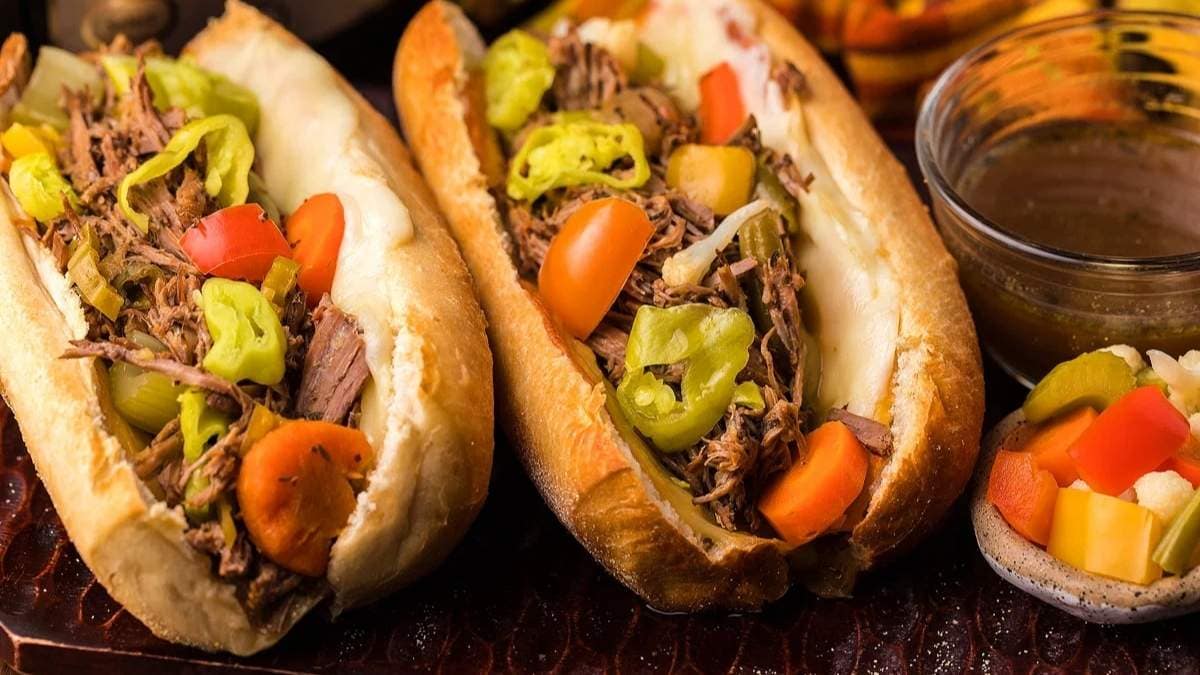 Two sandwiches with meat and vegetables on a wooden board.