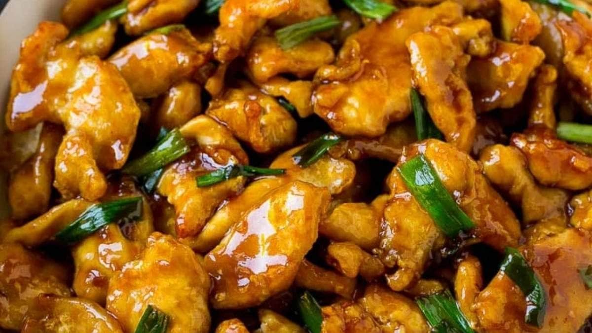 Chinese chicken in a white bowl with green onions.
